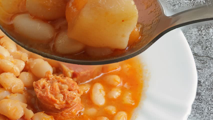 Close-up of a spoonful of white beans with a piece of cooked bacon; a healthy, high-protein meal.