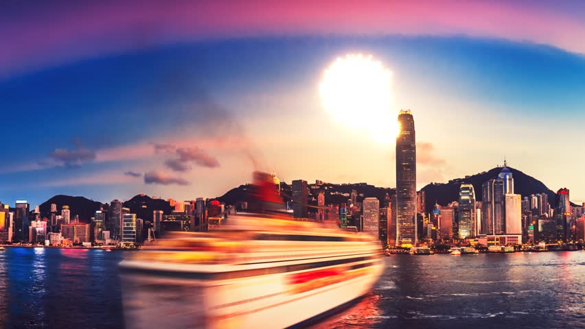 A vibrant cityscape captured by a long video sequence with a prominent boat moving across the water in Hong Kong