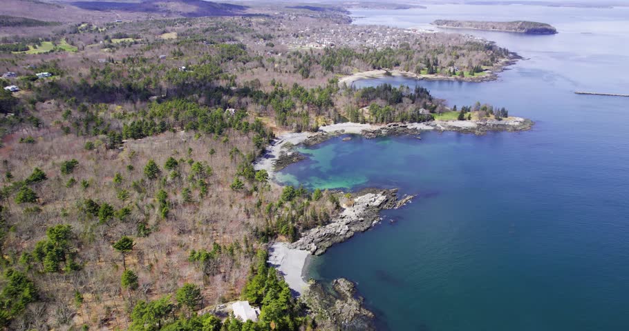 An elevated coastal view shows the rocky Atlantic shoreline and forested islands near Acadia Maine under clear daylight