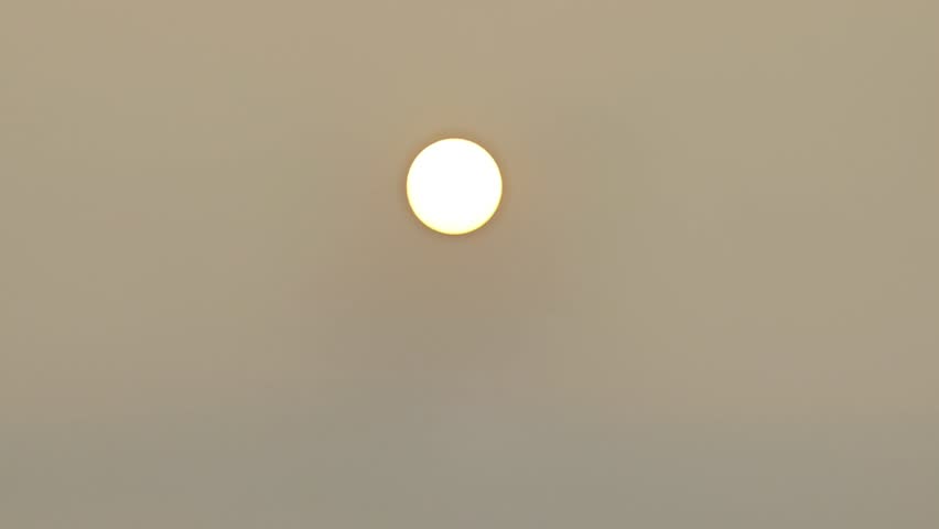 Bright glowing sun shining centered in a foggy, hazy, or misty sky during sunrise or sunset, creating a minimalistic and dramatic atmospheric background