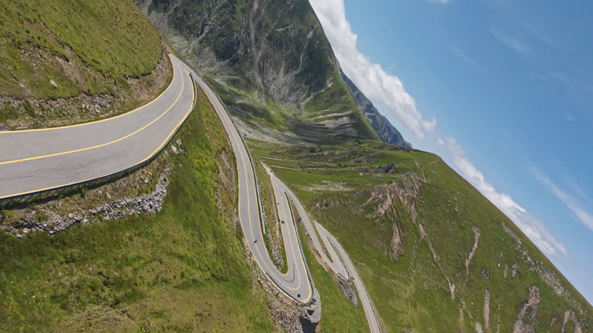 Dramatic Transalpina hairpin turns twist across steep green slopes above Plescoaia Valley in the scenic Romanian Carpathian Mountains.