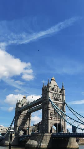 High-quality 4K vertical static video featuring cars and vehicle traffic driving across the historic Tower Bridge over the River Thames under a bright blue sky in London, England