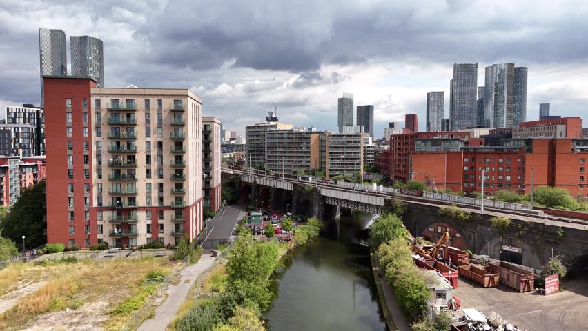 High buildings and railway tracks along the canal in the city of Manchester under a cloudy sky during the afternoon.