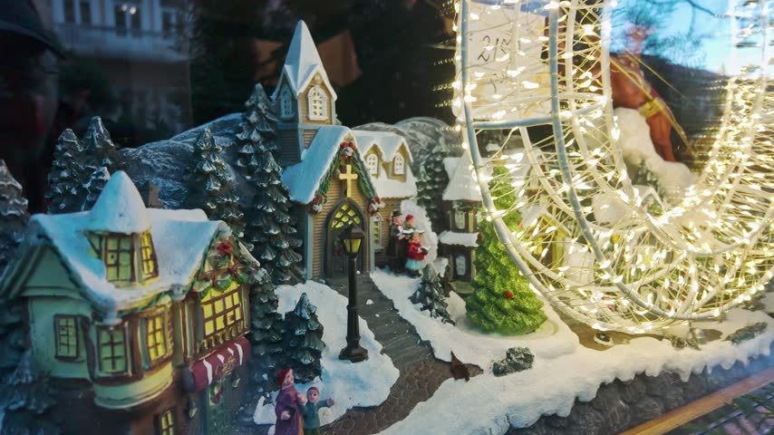 Charming miniature christmas village scene with snowy houses church carolers and glittering string lights.