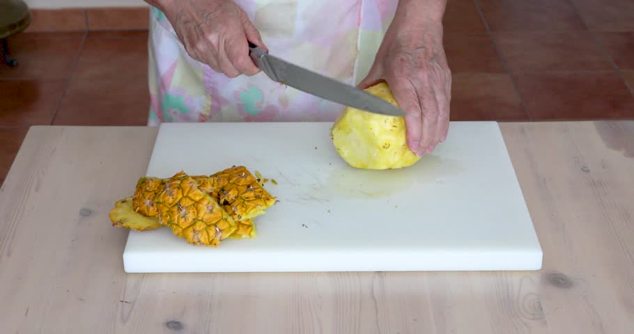 Slicing Peeled Fresh Pineapple into Round Pieces on White Cutting Board. Female hands cutting a peeled fresh pineapple into round slices with a kitchen knife on a white cutting board.