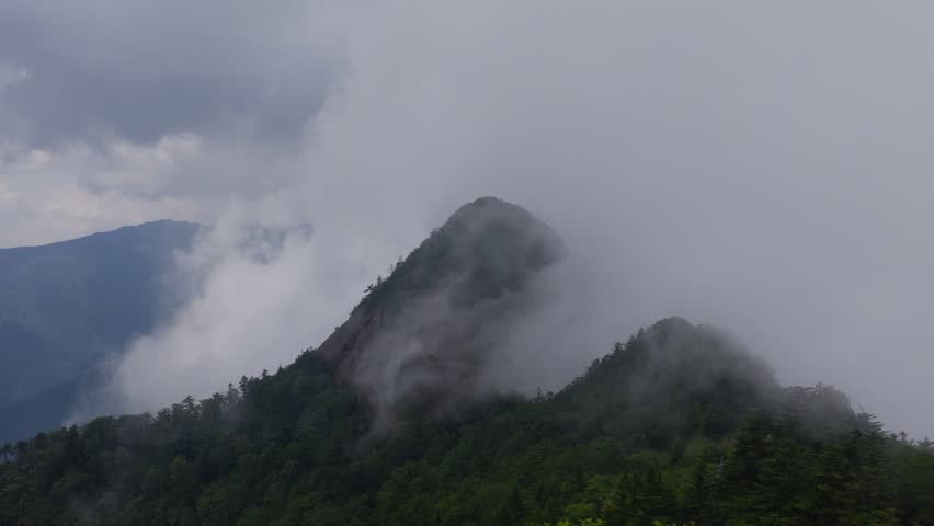 Fog and clouds move over green mountain peak on Shikoku, Japan
