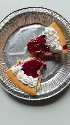 Detailed close up view of two slices of cherry strawberry jam cheesecake with whipped cream crust in aluminum foil pan on white background