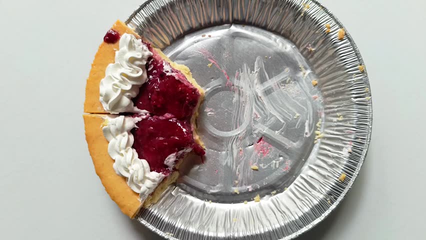 Two remaining slices of fruit cheesecake topped with red cherry strawberry jam and whipped cream in aluminum foil pie pan on white background