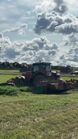 Red tractor mowing grass in field under dramatic cloudy sky jabuka Montenegro 