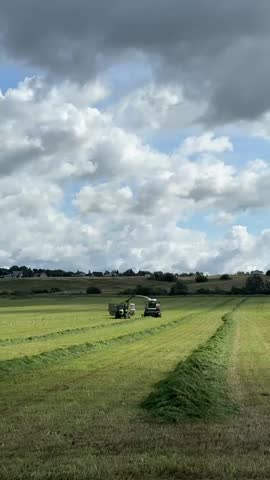 Farm tractors harvesting grass in large field under cloudy sky kempelevo russia