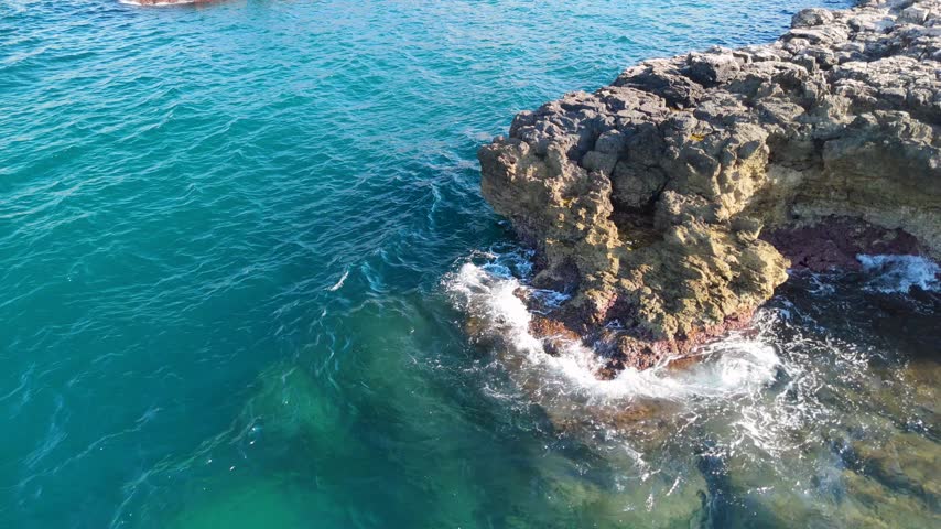 White sea foam forming around limestone rock ledge with turquoise water washing over the shallow rocky bottom