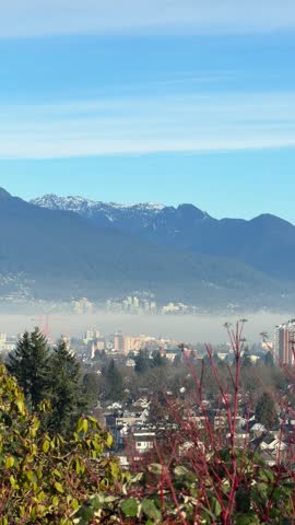 Vancouver city skyline with snow-capped mountains and morning fog viewed from Queen Elizabeth Park, showing cityscape, buildings and North Shore mountains.