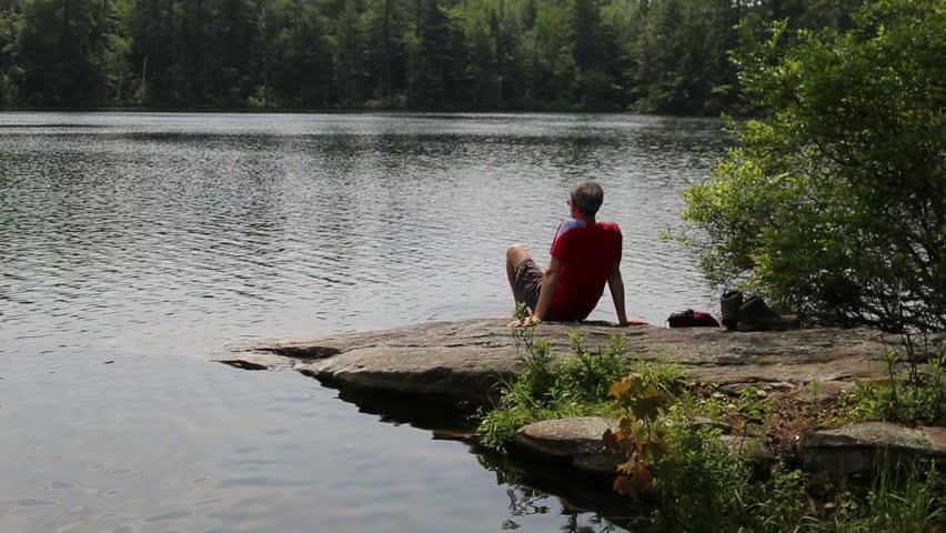 Hiker relaxing at the edge of a secluded mountain pond.  Cole pond, Enfield, New Hampshire.