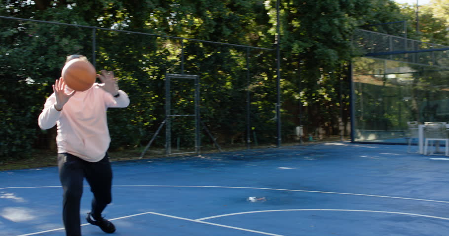 Diverse males playing at backyard court hoodie tossing basketball African American shooting layup. Outdoor, hoop, net, ball, fence, trees, sunshine