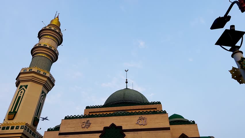 An airplane flying over the golden-colored mosque against clear blue sky.