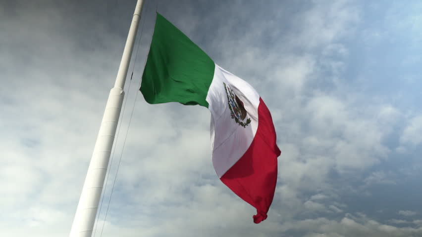 Tricolor Mexican Flag slowly Waving in Wind Against Dramatic Cloudy Sky look up closeup view