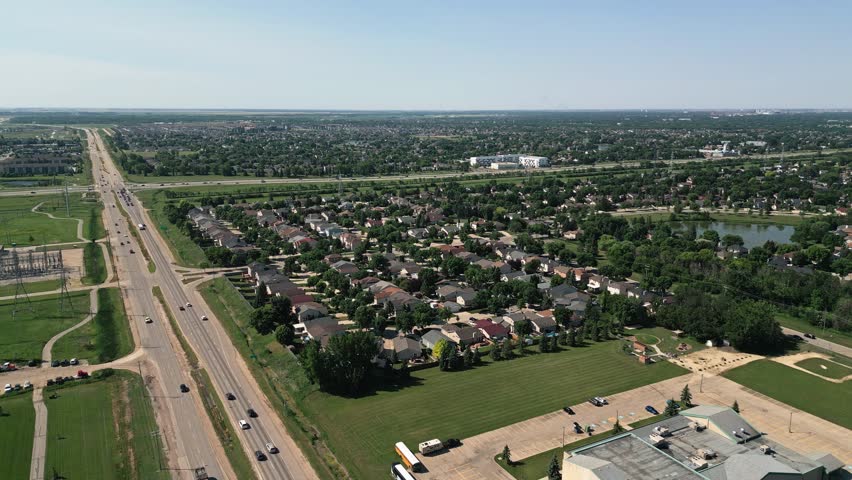 Aerial drone shot of residential homes beside a major roadway and intersection in Winnipeg, Manitoba on a bright summer day