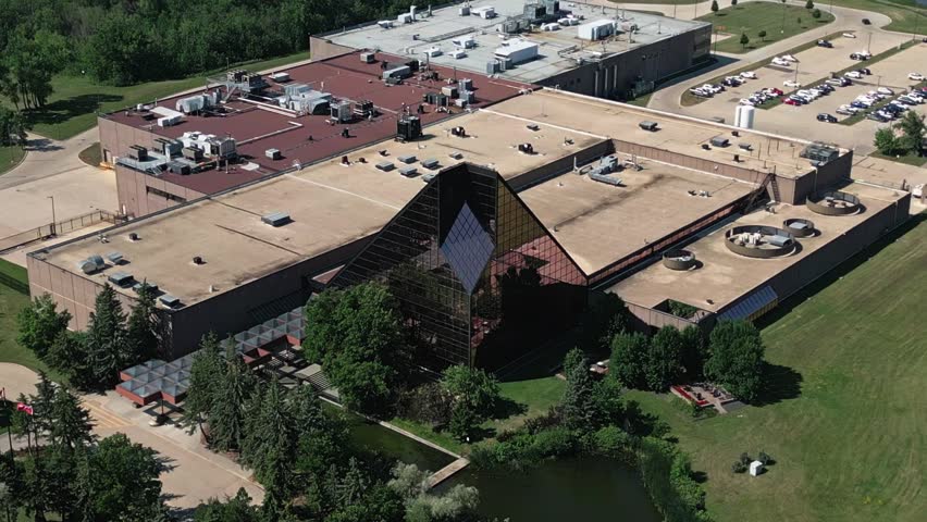 Static telephoto drone shot of the glass entrance pavilion at the Royal Canadian Mint in Winnipeg, Manitoba on a bright summer day