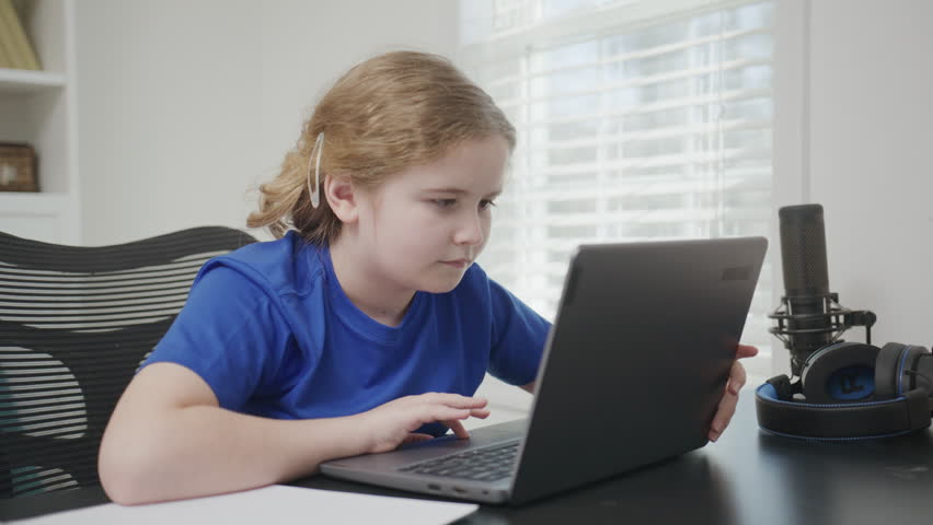 Excited school child using laptop computer. Child online learning with laptop at home class. School child studying at home. Kid using a laptop computer, studying online. Home schooling concept.