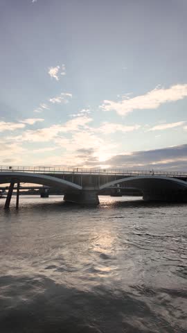 Grosvenor Bridge spans the River Thames as low sun glare ripples across moving water. vertical video, slow motion