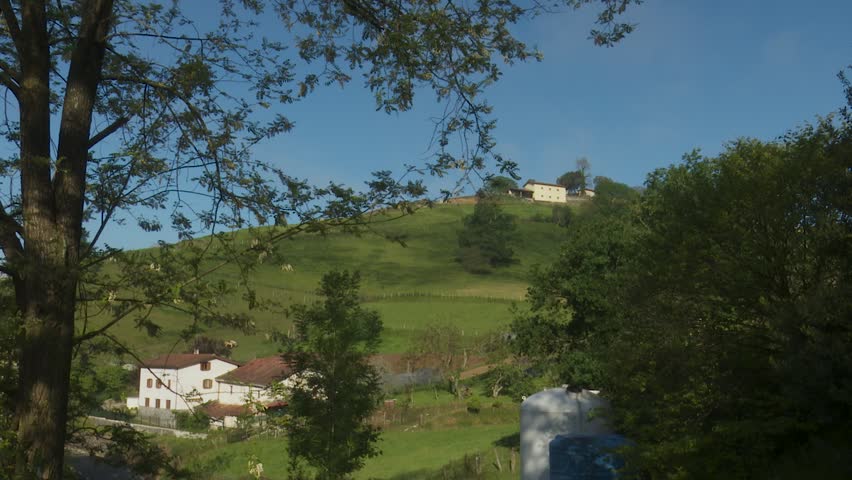 Rural landscape with white farmhouse and green hillside under sunny sky