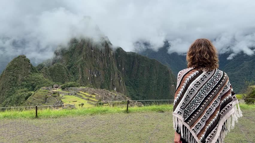 Tourist woman wearing traditional poncho visiting Machu Picchu in Peru