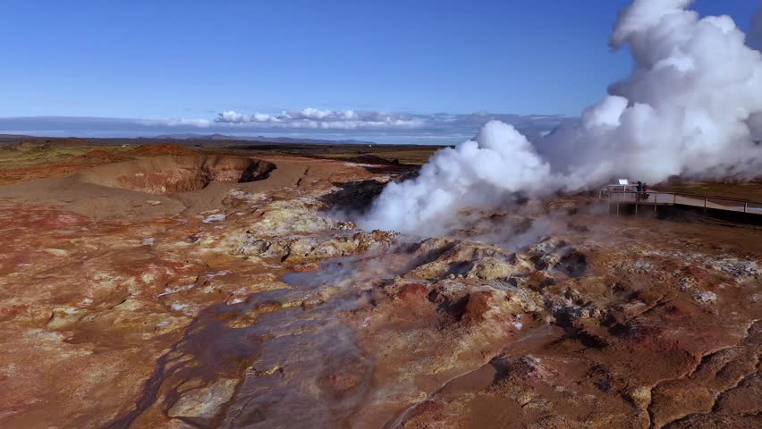 Aerial drone view of a steaming geothermal field near Lake Myvatn in North Iceland featuring active steam vents mineral rich ground hot springs and visitors on a wooden walkway