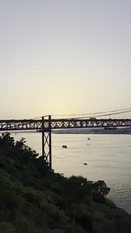 25 de Abril suspension bridge over the Tagus River in Lisbon, Portugal, at sunset with calm water and clear sky.