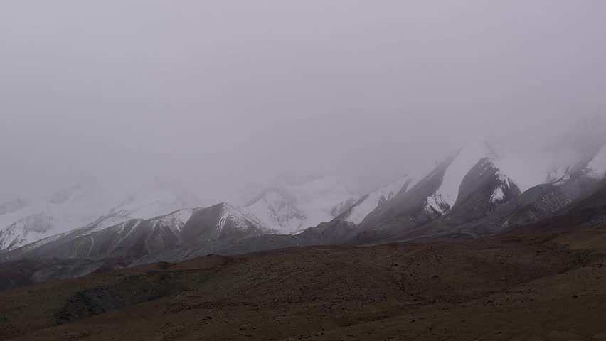 Majestic snow capped mountain range covered in heavy fog and overcast mist in high altitude terrain.