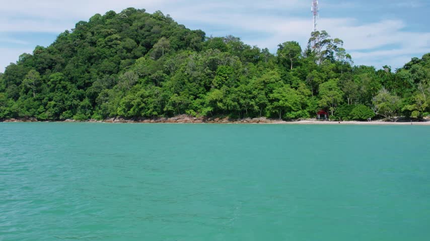 Smooth cinematic drone footage creating a beautiful parallax effect as a lush tropical shoreline slowly recedes behind vibrant turquoise waters.