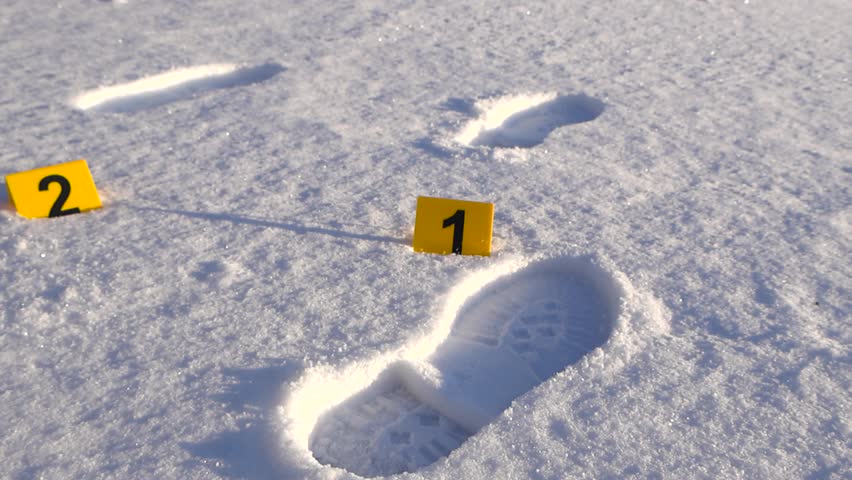 Evidence markers numbered one and two positioned on snowy ground marking footprints at outdoor crime scene. Cinematic footage capturing forensic investigation detail in winter environment.