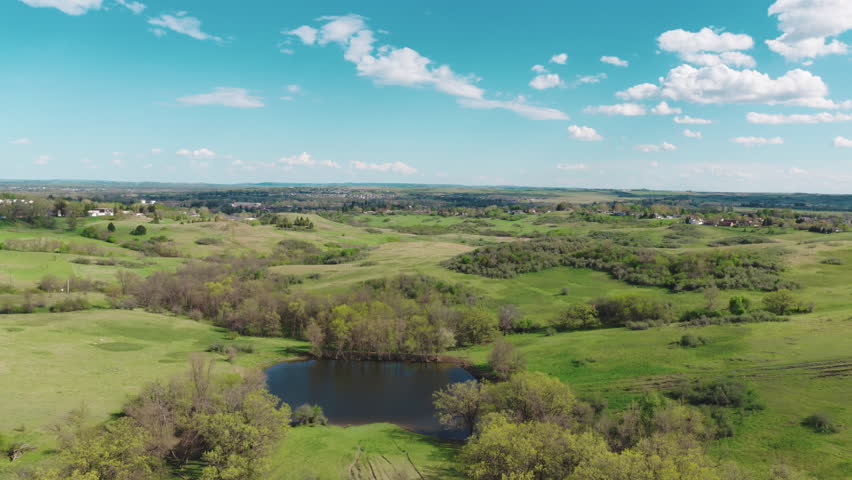 Small prairie town nestled among green rolling hills under a blue sky with cumulus clouds in North Dakota, spring.