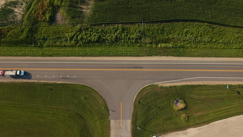 Aerial topdown shot of a two lane rural highway in Shiocton, Wisconsin, featuring semi-truck with a trailer and passenger cars driving past green farm fields.