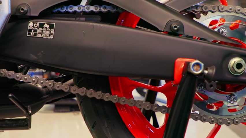 Close-up video of a modern sports motorcycle rear wheel with red rim, chain, sprocket, swingarm, and rear paddock stand.