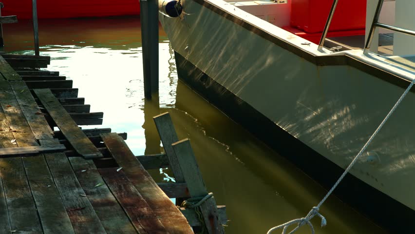Boat hull docked alongside a weathered wooden jetty at day, water rippling in lake.