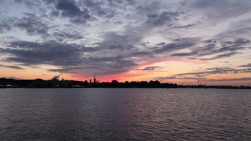 Time lapse of a spectacular summer sunrise over the IJ waterfront and port area in Amsterdam, Netherlands. Colorful morning sky with dramatic clouds reflecting warm sunlight over the water.