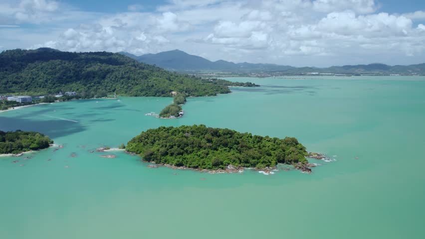 Drone footage capturing an idyllic island landscape framed by calm turquoise sea, distant mountains, and the breathtaking scenery of Langkawi, Malaysia.
