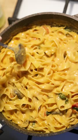 Creamy Italian pasta with mushrooms and fresh tomatoes in a rich sauce, served in a skillet and prepared at home, creating an appetizing rustic meal with vibrant colors and fresh ingredients