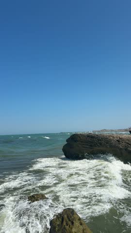 Large coastal rocks with waves crashing against the shoreline on a windy day, Caspian Sea under a clear blue sky