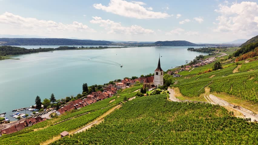 Ligerz, Lake Biel, Bern, Switzerland, revealing St. Peter Church, terraced vineyards, the lakeside village, turquoise freshwater and the Swiss Plateau, drone slide.