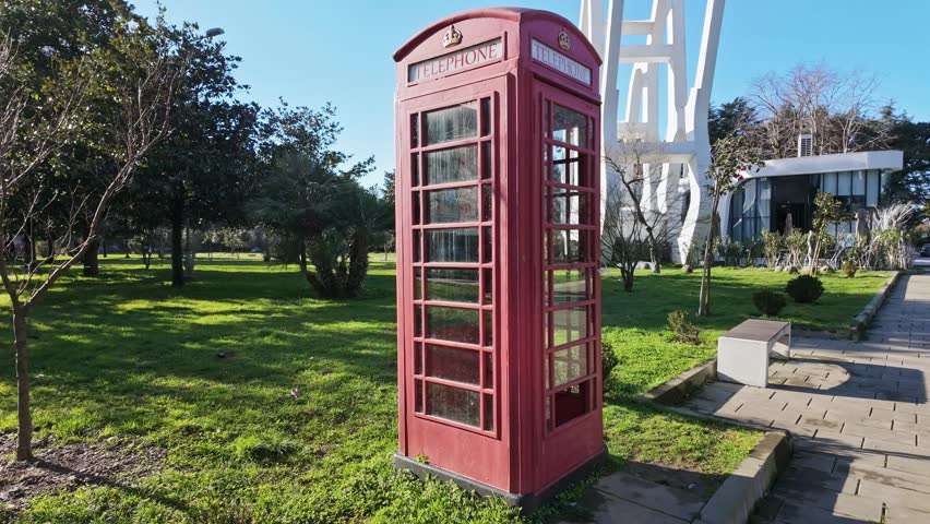 Classic red british style telephone booth stands in a sunny green park in batumi georgia.