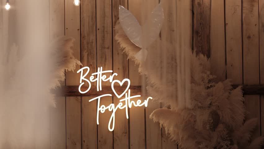Illuminated Better Together neon sign mounted on a rustic wooden wall surrounded by pampas grass