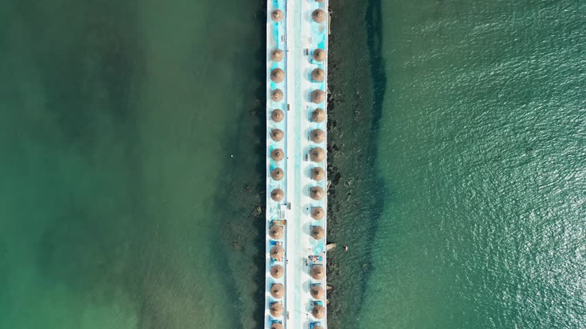 Albania, Durres 07 09 2025: Symmetrical top-down drone video moving forward along a pier pathway over the sea until revealing the Hawaii Beach Club in the center.