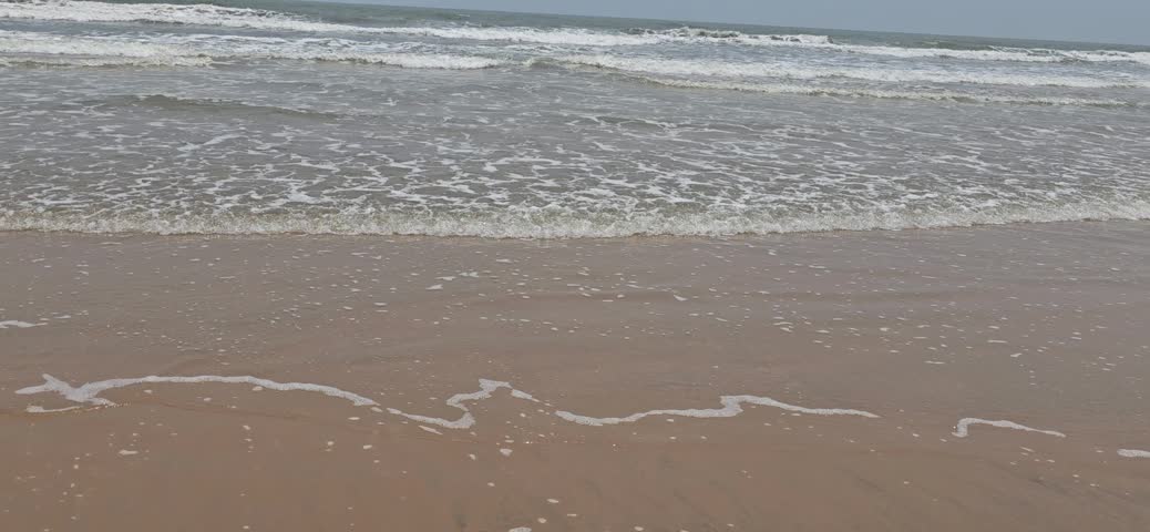 Gentle ocean waves washing onto sandy beach shoreline with white foam