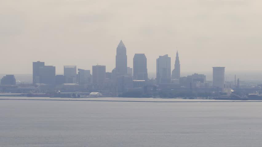 Cleveland, OH skyline with cloudy moody sky above on overcast summer day as tall buildings, skyscrapers, office building, and structures in silhouette stand over Lake Erie on Ohio coastline 4k
