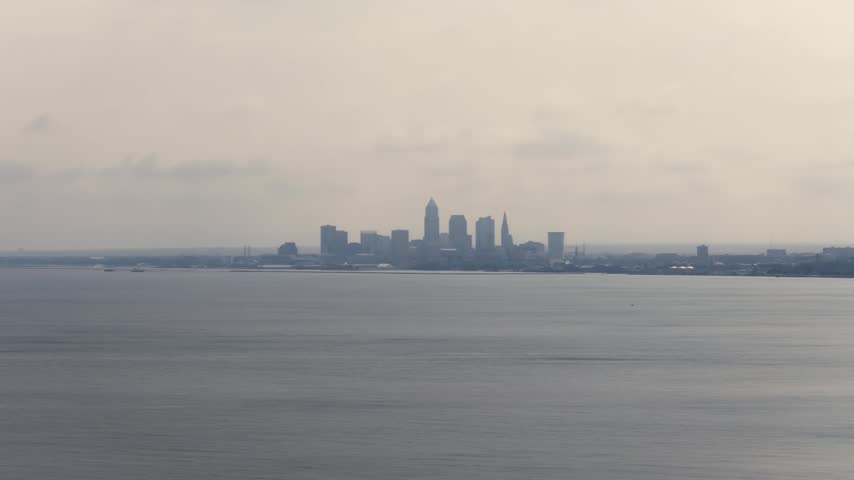 Cleveland, OH skyline with cloudy moody sky above on overcast summer day as tall buildings, skyscrapers, office building, and structures in silhouette stand over Lake Erie on Ohio coastline 4k