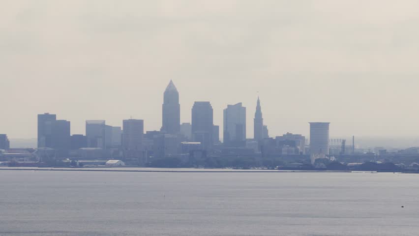 Cleveland, OH skyline with cloudy moody sky above on overcast summer day as tall buildings, skyscrapers, office building, and structures in silhouette stand over Lake Erie on Ohio coastline 4k