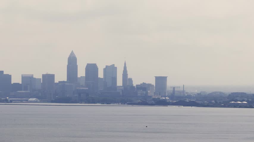 Cleveland, OH skyline with cloudy moody sky above on overcast summer day as tall buildings, skyscrapers, office building, and structures in silhouette stand over Lake Erie on Ohio coastline 4k