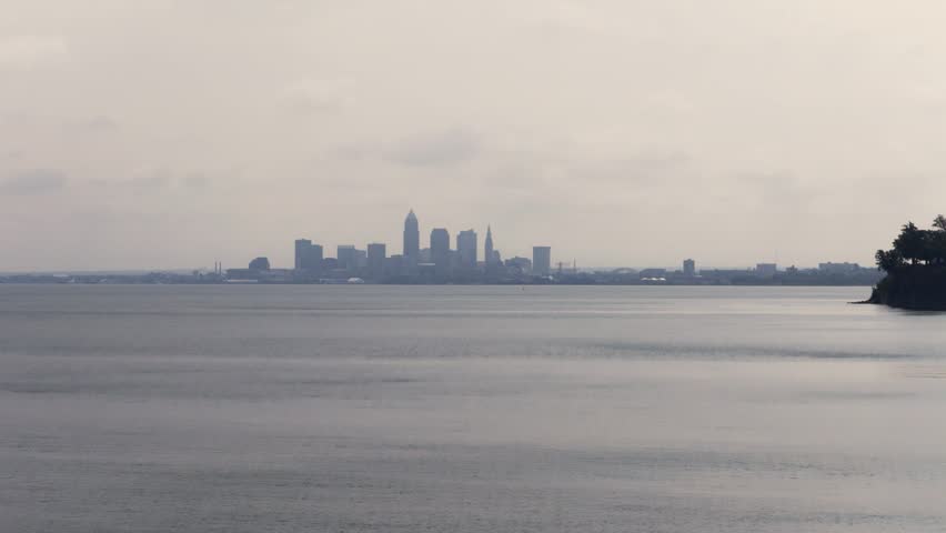 Cleveland, OH skyline with cloudy moody sky above on overcast summer day as tall buildings, skyscrapers, office building, and structures in silhouette stand over Lake Erie on Ohio coastline 4k