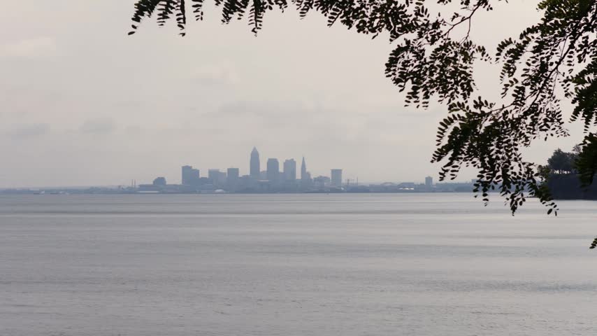 Cleveland, OH skyline with cloudy moody sky above on overcast summer day as tall buildings, skyscrapers, office building, and structures in silhouette stand over Lake Erie on Ohio coastline 4k